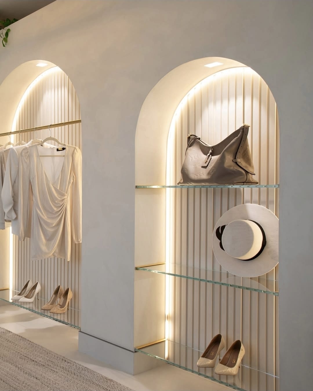 Two arched retail niches with warm perimeter LED lighting, fluted backs, garments, and glass shelves.