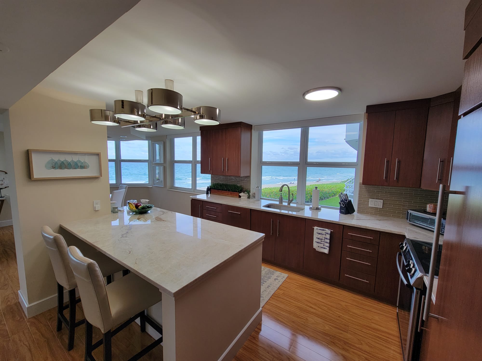 Modern kitchen with multi-head chrome chandelier over a marble island and large windows.