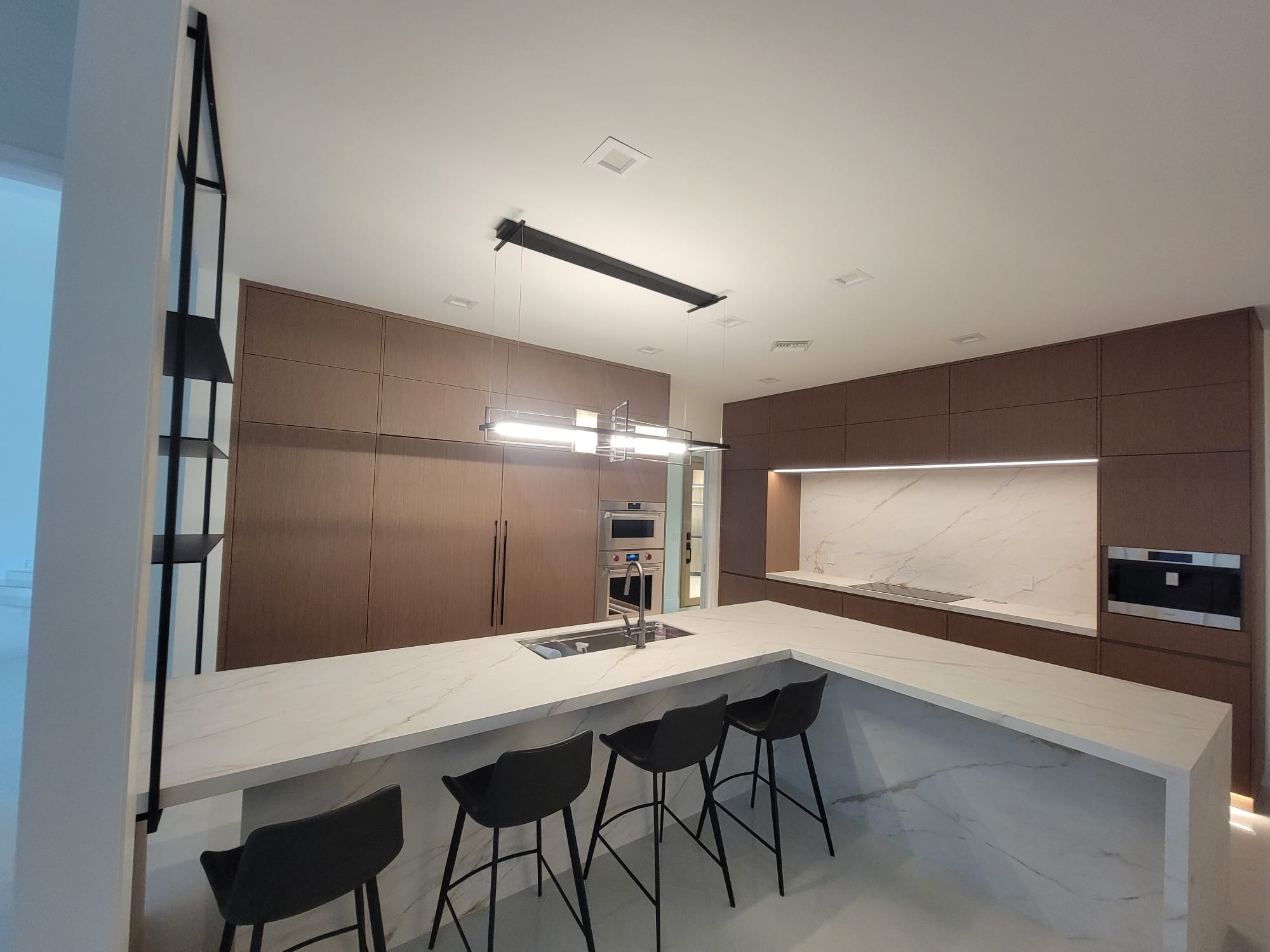 Contemporary kitchen with dark wood cabinets, white marble island, and dual-tube black pendant.
