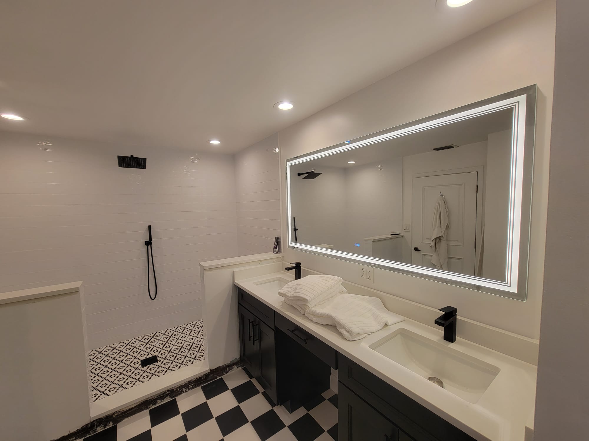 Bathroom with LED-bordered vanity mirror, recessed ceiling lights, and checkered tile floor.