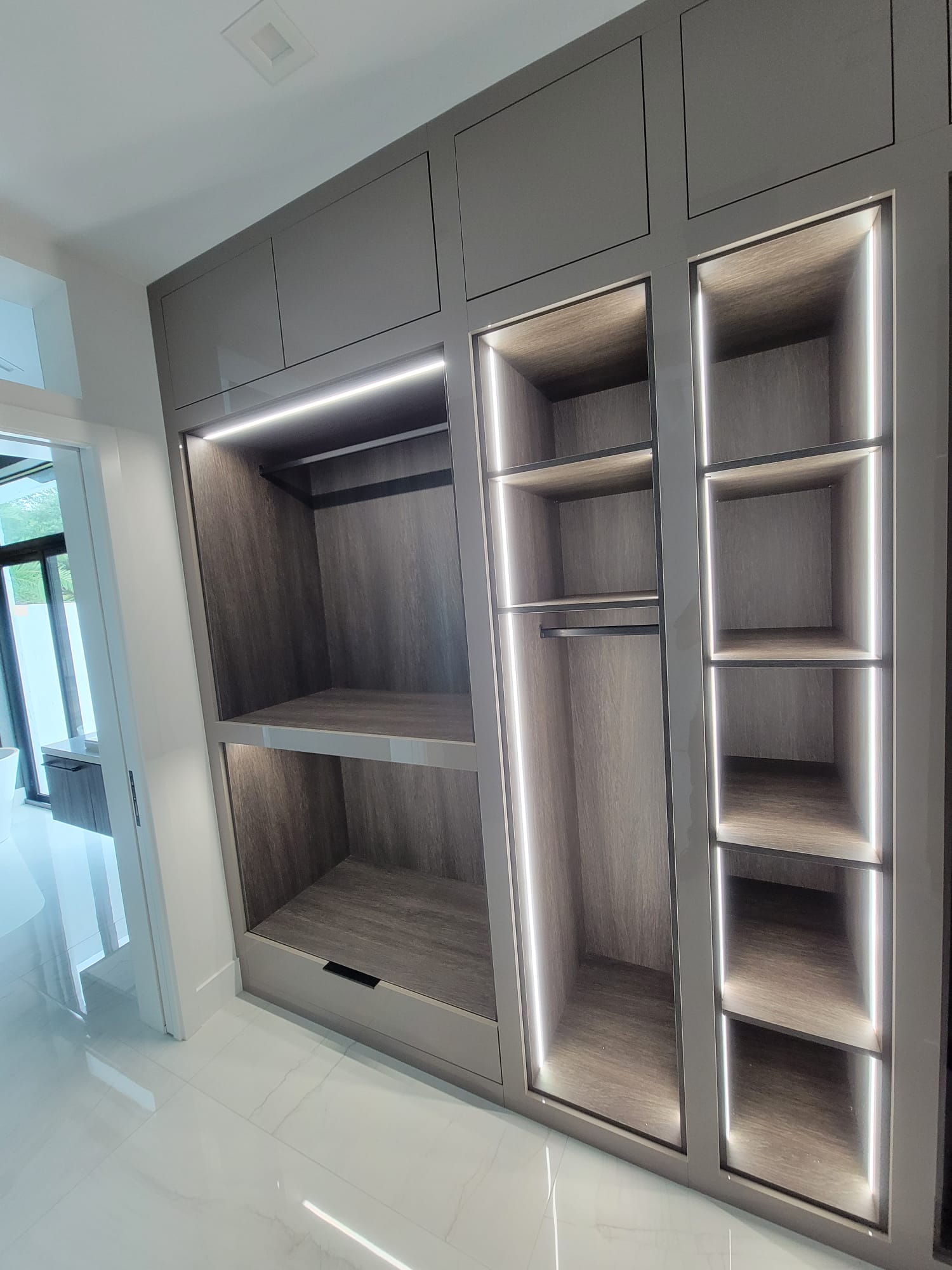 Walk-in closet with glossy cabinets and wood interiors lit by recessed linear LED strips.