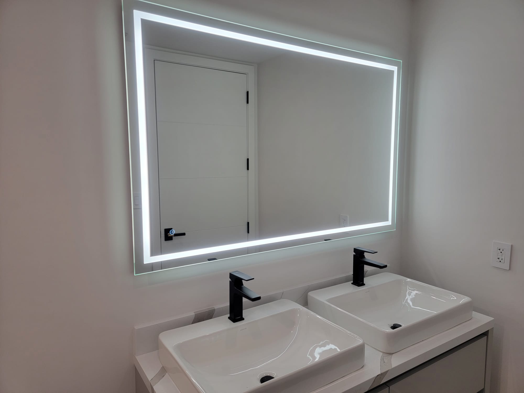 Bathroom vanity with a large rectangular LED-border mirror above two white vessel sinks.