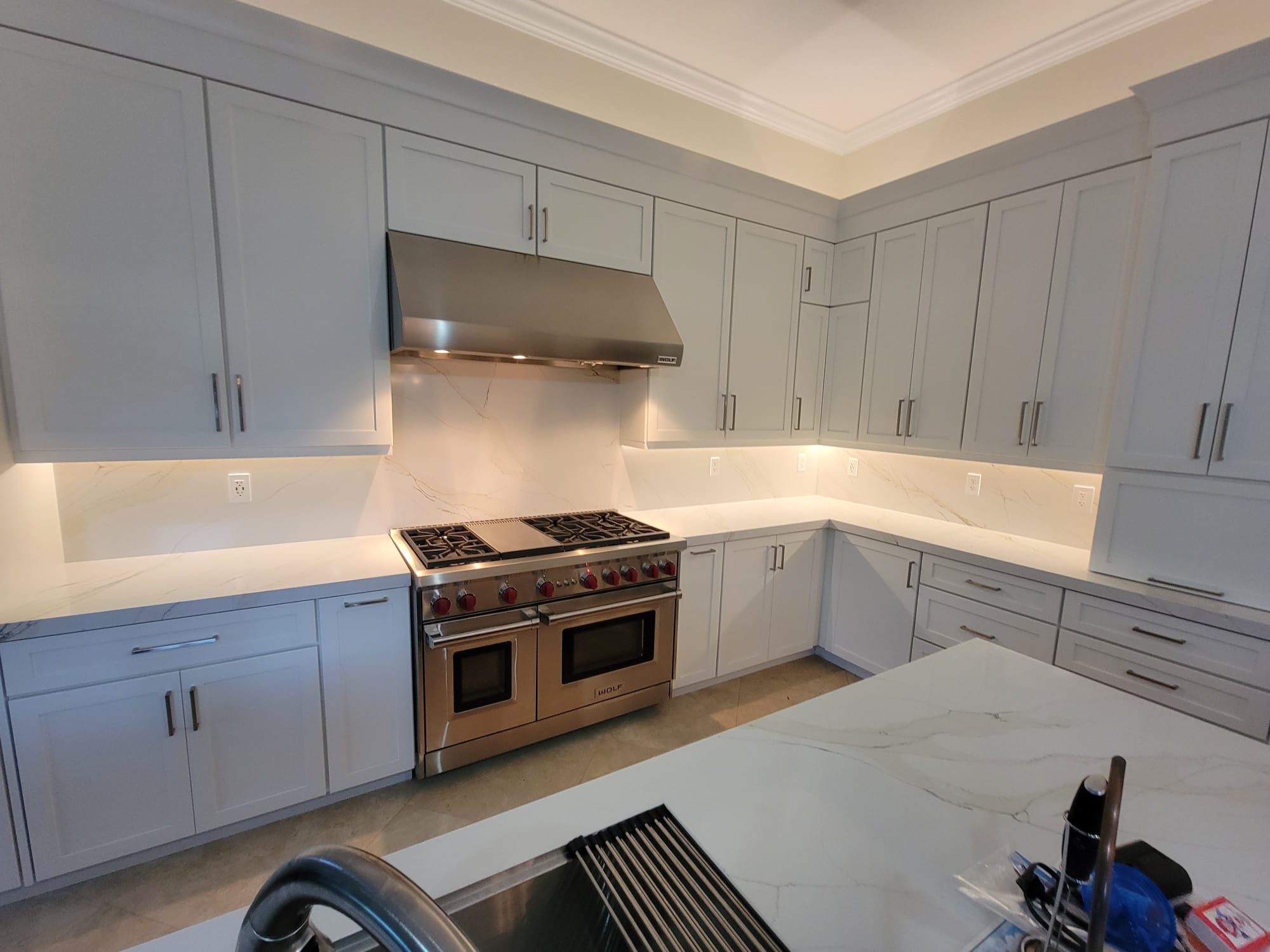 L-shaped kitchen with light gray cabinetry, white marble surfaces, and under-cabinet LED glow.