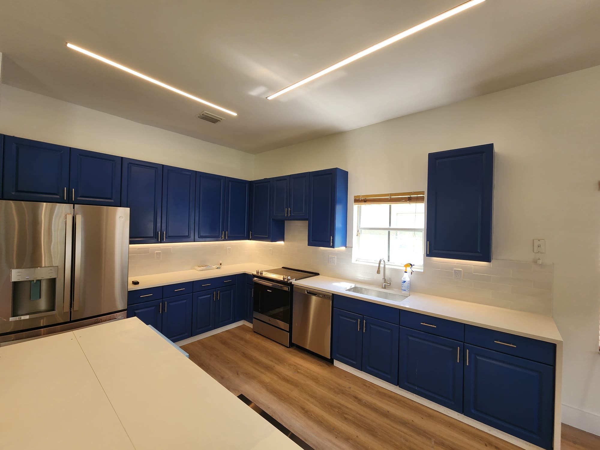 Modern kitchen with blue cabinets, linear ceiling LED strips, under-cabinet lighting, and stainless appliances.
