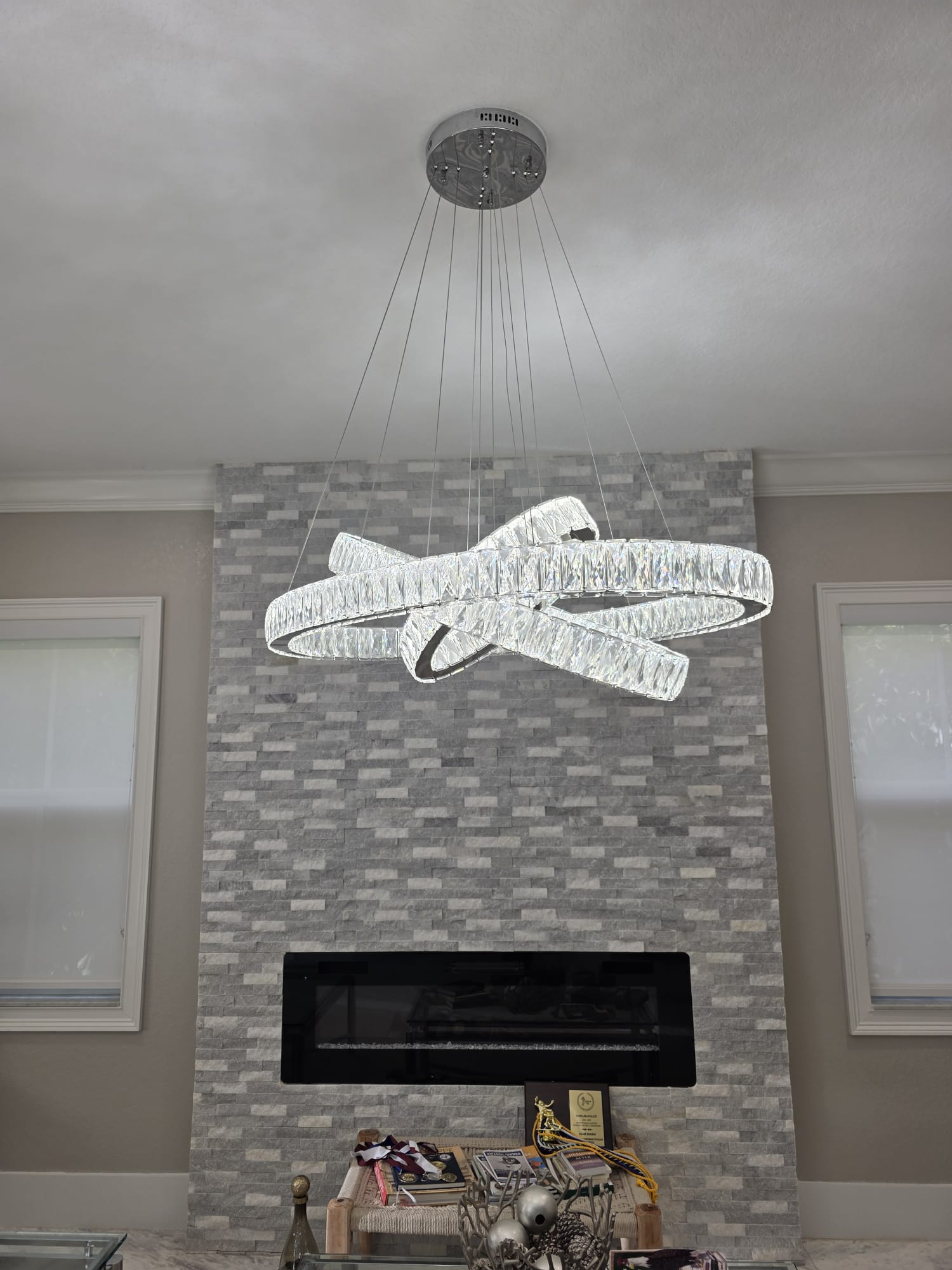 Living room with a three-ring crystal chandelier before a stone fireplace between tall windows.