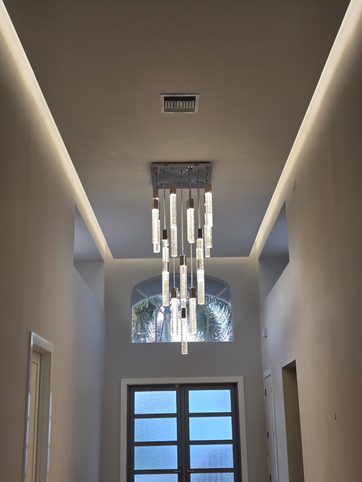 High foyer with staggered glass cylinder chandelier, cove LEDs, and frosted double doors.