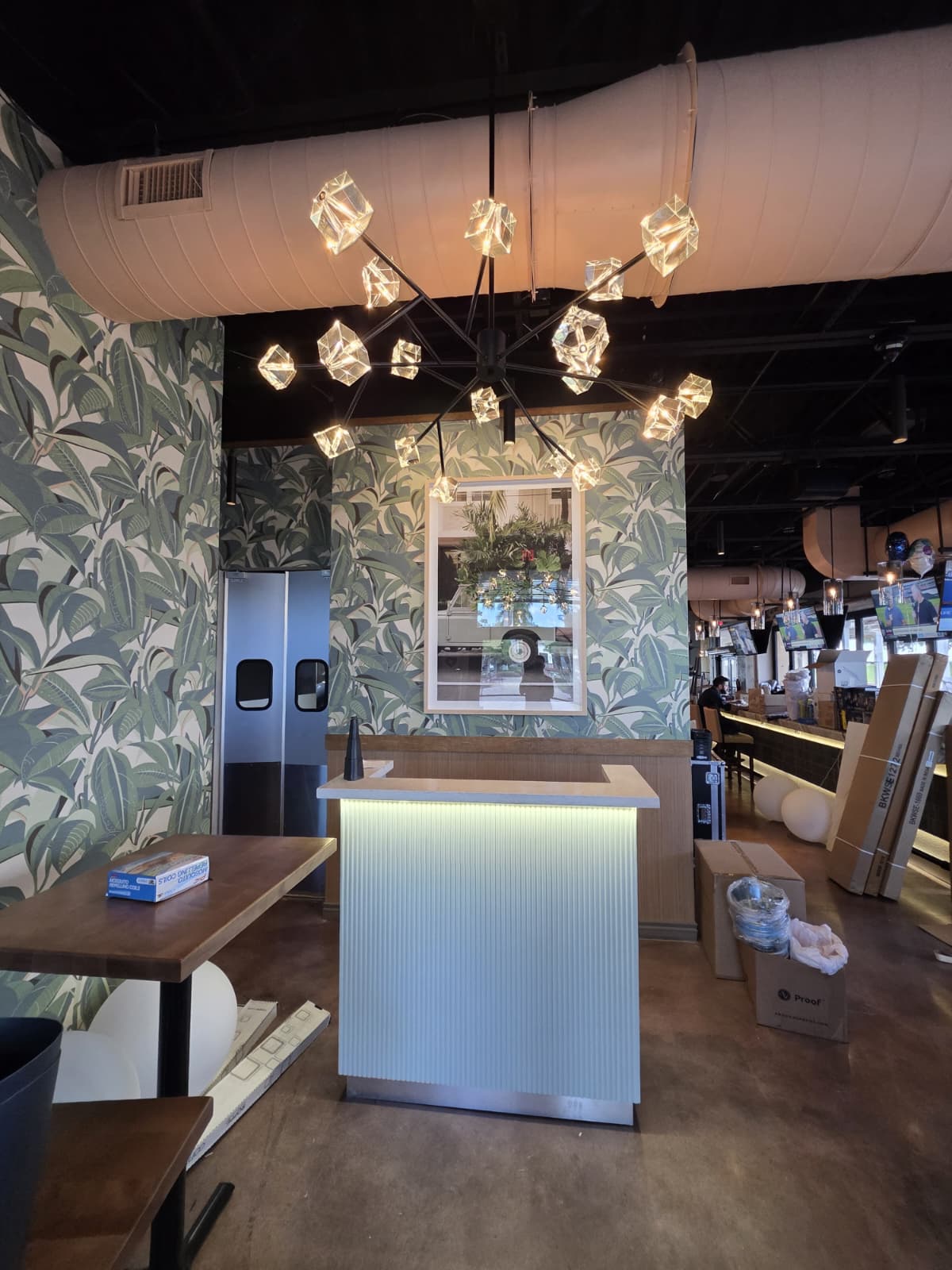 Black multi-arm chandelier with cube glass shades over a fluted white reception desk with integrated LED edge lighting.