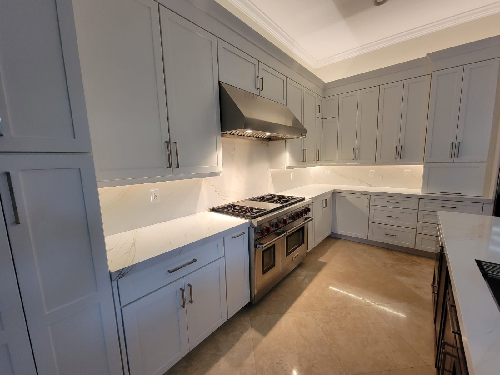 Light-gray kitchen with white stone counters, under-cabinet LED glow, and stainless range with illuminated hood.