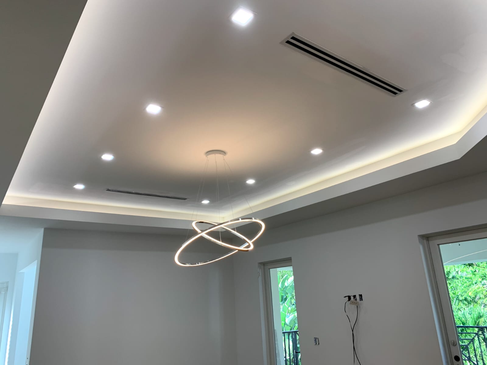 Tray ceiling with dual glowing ring pendants, cove LEDs, and square recessed downlights.